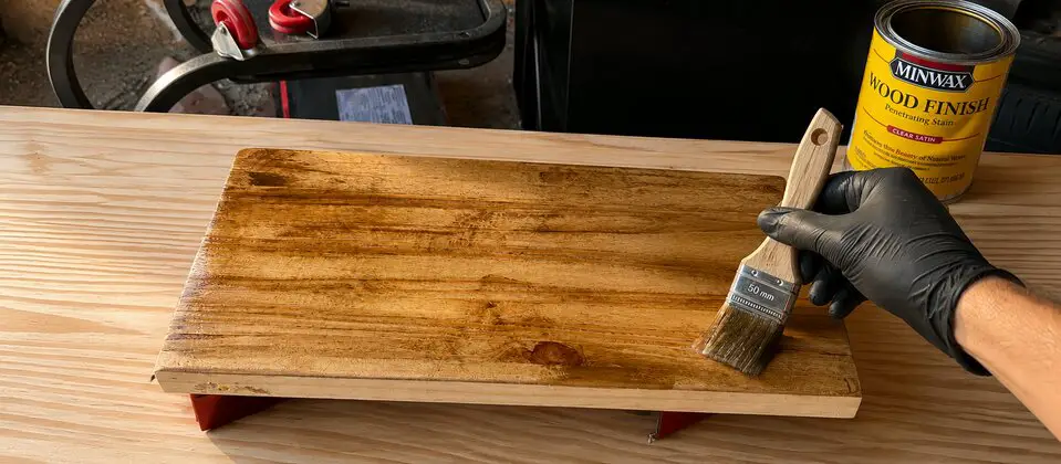 Applying a clear finish to an oak surface in a woodworking workshop with raking light revealing the grain